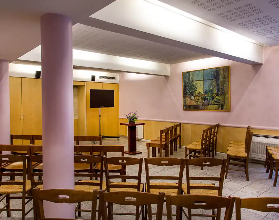 CPL-Salles-Formigé-3 Salle de cérémonie lumineuse avec chaises en bois, pupitre central, écran et tableau mural dans un espace épuré