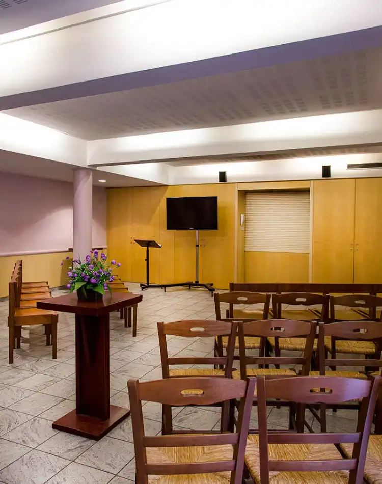 CPL-Salles-Formigé-4 Salle de cérémonie intimiste avec chaises en bois, pupitre fleuri et écran, dans un espace moderne et apaisant