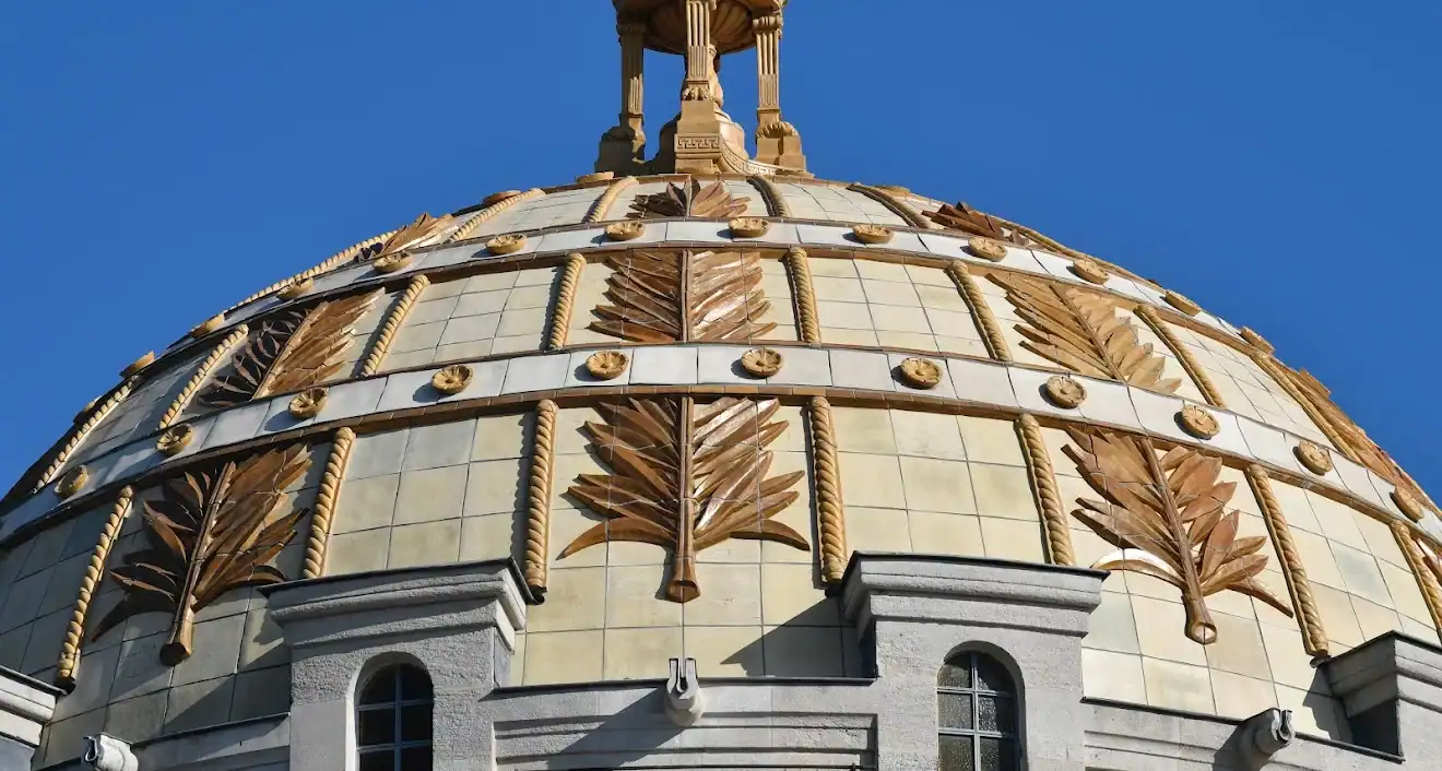 CPL-image-coupole-exterieur-2 Détail de la coupole ornée de motifs végétaux dorés, se détachant sur un ciel bleu, au sommet d’un édifice architectural élégant